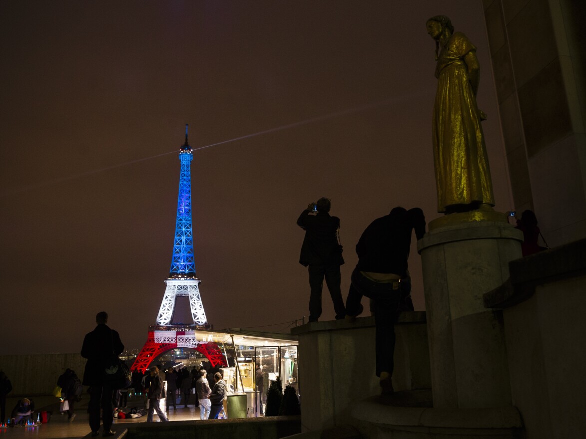 A man takes a picture of the Eiffel Tower illuminated in the French colors in honor of the victims of the attacks on Friday in Paris.